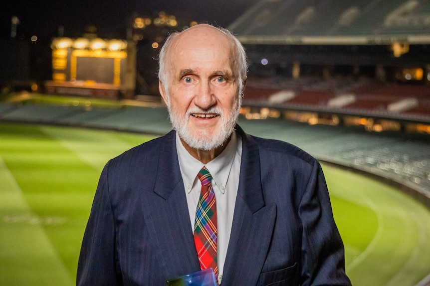 A man with a white beard and bald head wearing a suit and holding an award