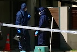 Forensic police in blue jumpsuits and masks outside a home cordoned off with police tape.