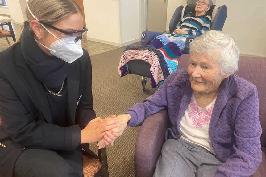 teenager holding the hand of an old lady, sitting and smiling