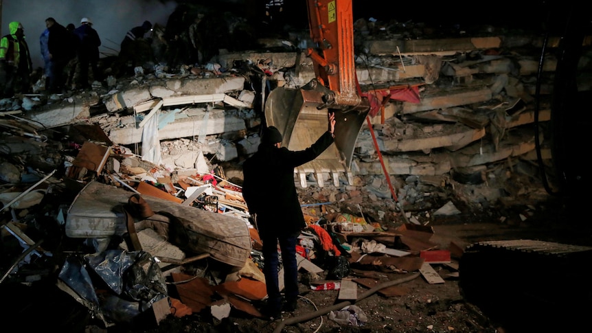 A man stands in front of a collapsed building