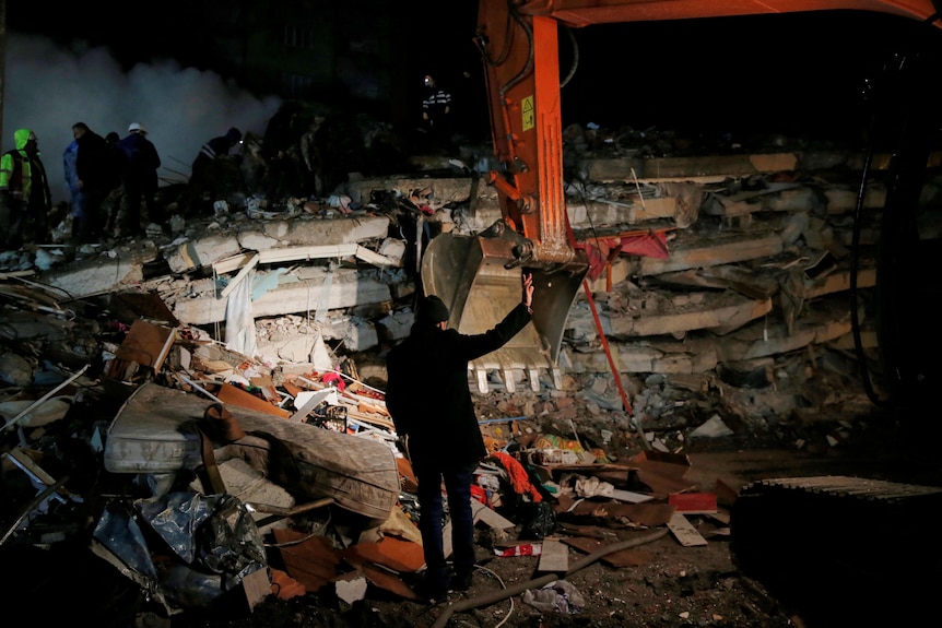 A man stands in front of a collapsed building