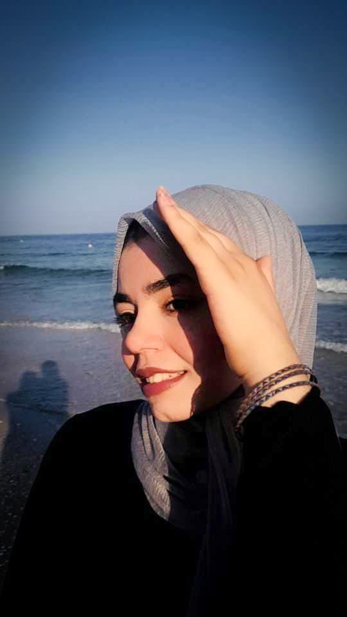 A close up of a woman hiding her face from the sun on a beach.