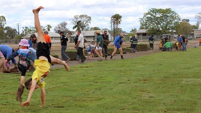 A young student does cartwheel on new turf with volunteers laying turf in background.