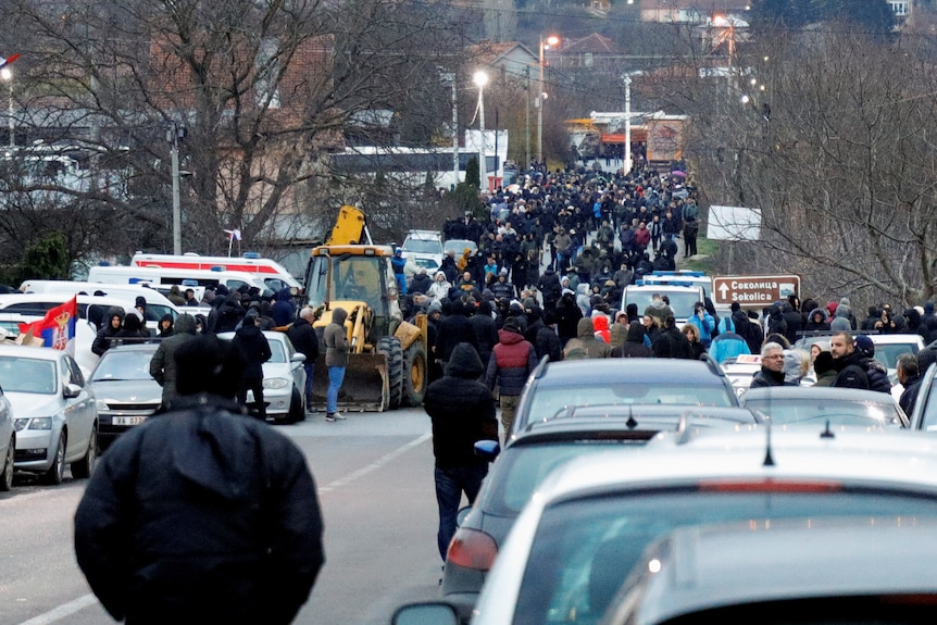 people stand in the middle of a road in Kosovo as cars are banked up along the road