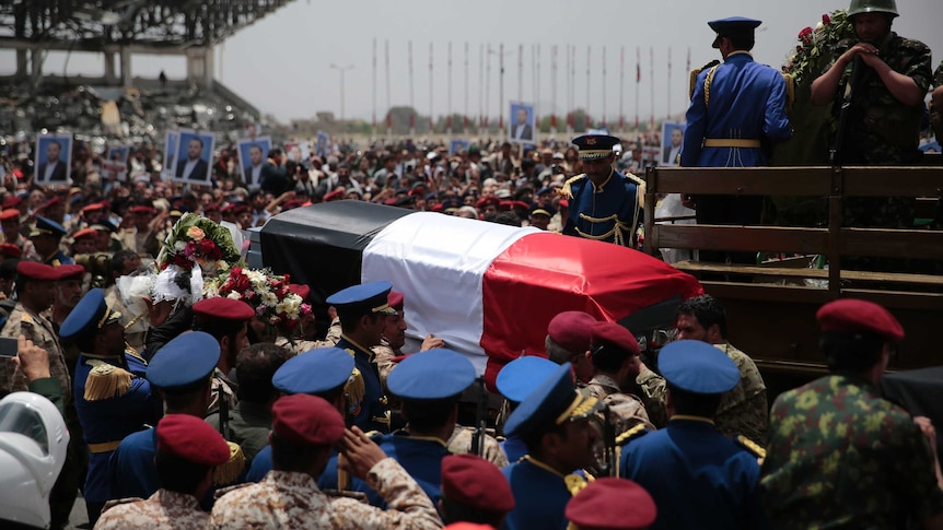 Guard salute as others carry coffin draped in Yemen flag.