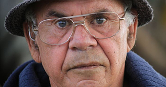 A man wearing glasses and a bucket hat stares deeply at the camera while having his portrait taken.