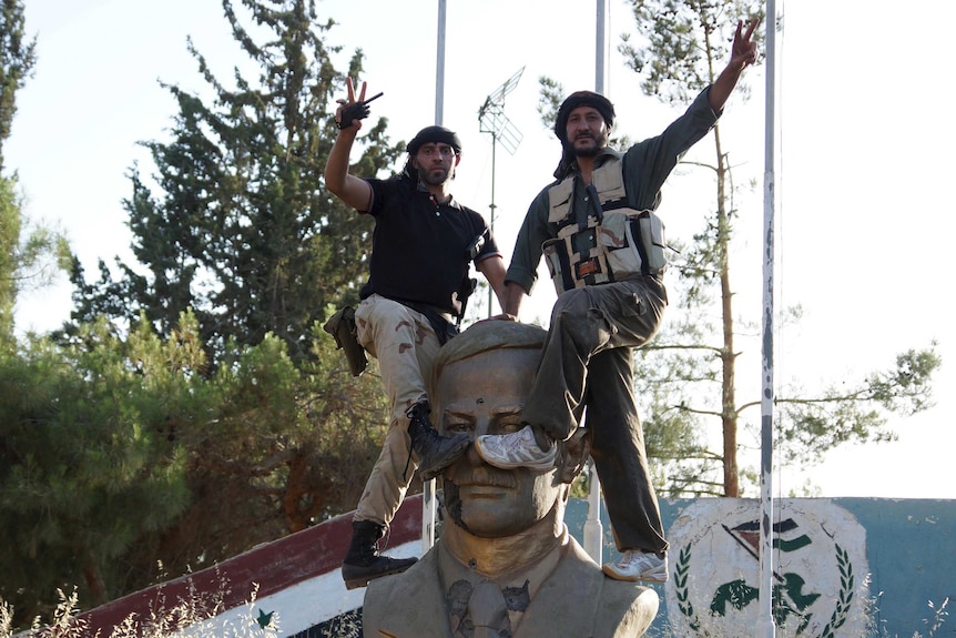 Free Syrian Army members climb on a sculpture of late Syrian president Hafez al-Assad