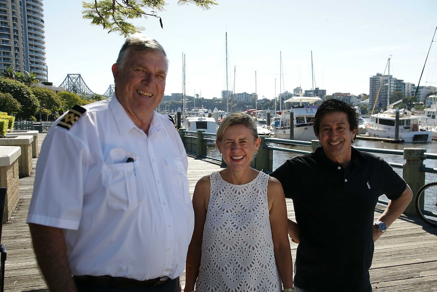 Two men and a woman stand on a timber deck pathway by a marina