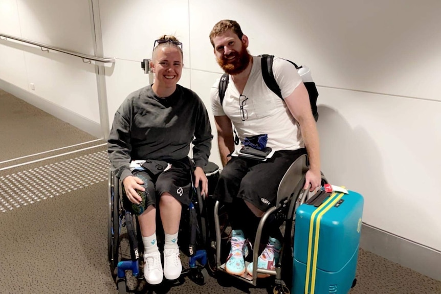 Smiling woman and man in wheelchairs with suitcase in airport hallway