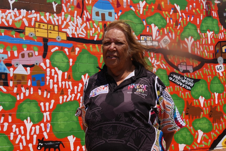 A woman stands in front of a colourful mural