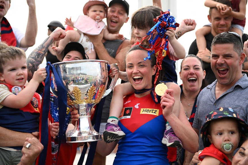 Daisy Pearce holds the premiership cup while standing with members of the crowd and holding her daughter on her shoulders