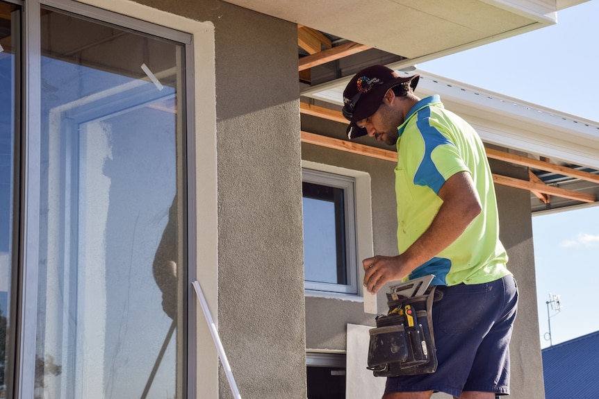 Man stands on ladder near roof and gets tools out of his pouch on his hips