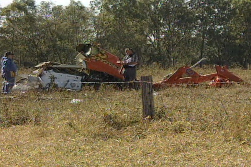 Two people inspect the crash site of a helicopter destroyed in a paddock.