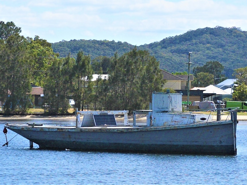 small, rundown, timber tug boat moored on water