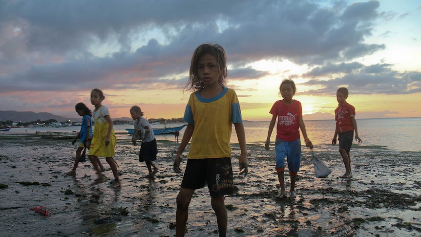 A group of children stand on a beach in Timor-Leste at sunset