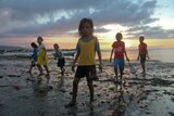 A group of children stand on a beach in Timor-Leste at sunset