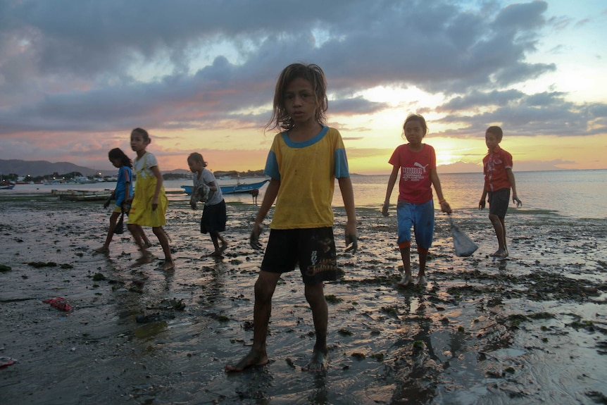 A group of children stand on a beach in Timor-Leste at sunset