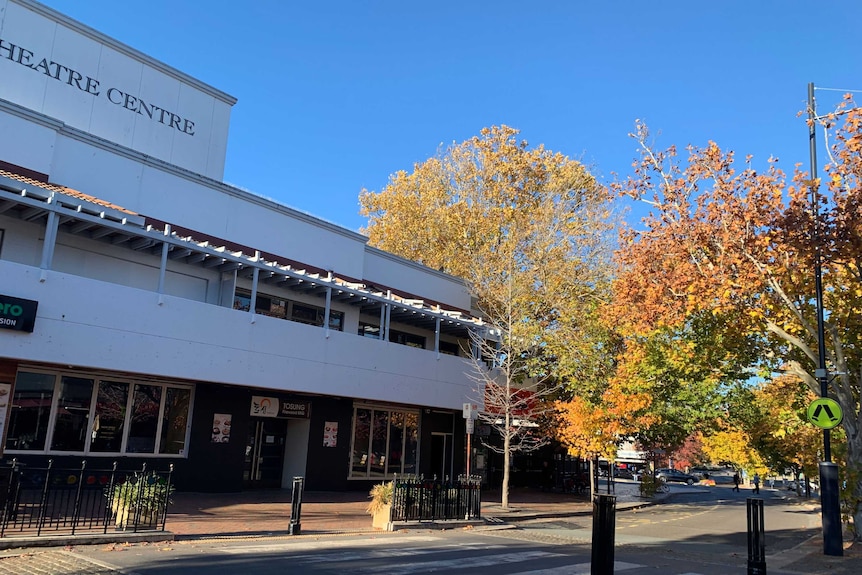 Autumnal trees stand next to a theatre near a street running through Manuka.