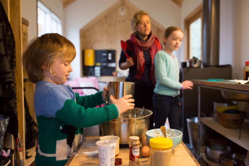 A woman and two children cooking in a small kitchen.