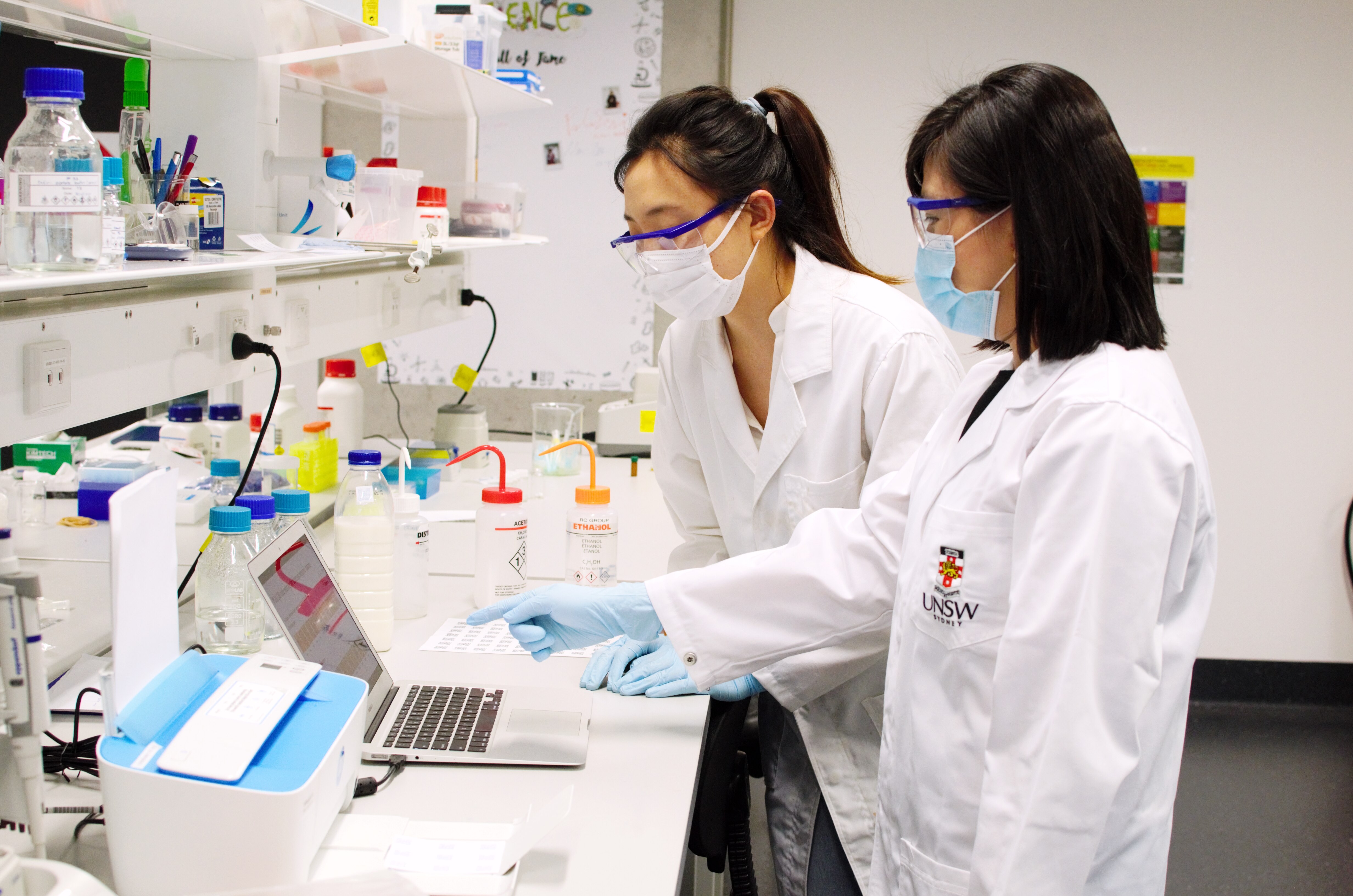 Two women in lab jackets looking to the left in a lab.
