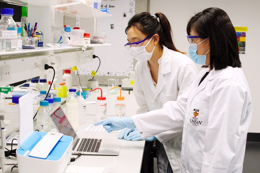 Two women in lab jackets looking to the left in a lab.
