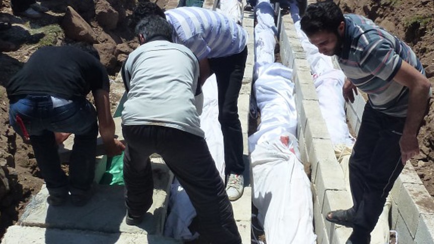 People watch the mass burial of more than 100 victims killed in the central Syrian city of Houla.