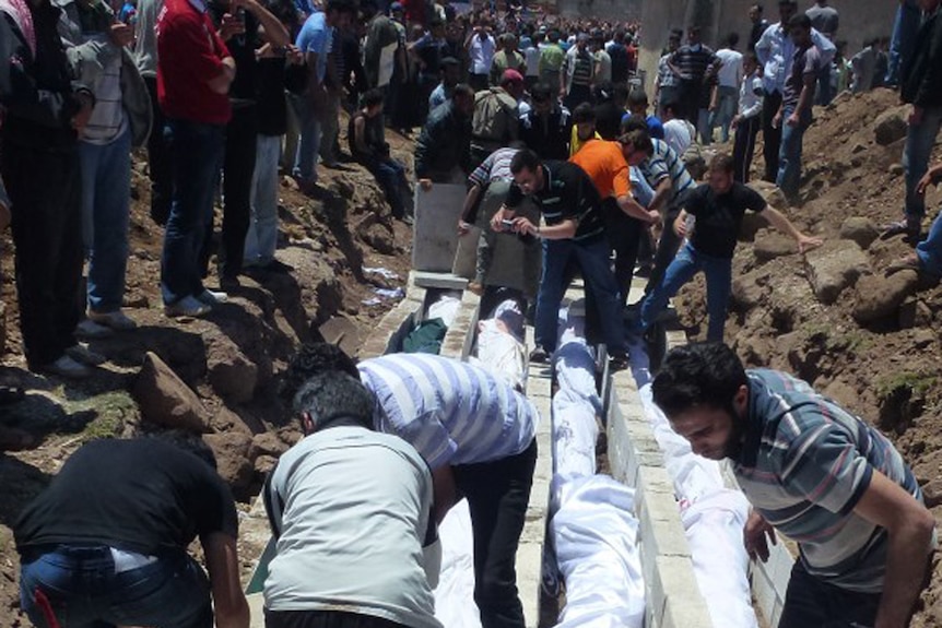 People watch the mass burial of more than 100 victims killed in the central Syrian city of Houla.