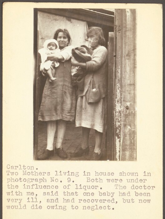 An old photo of two women in a slum holding babies.