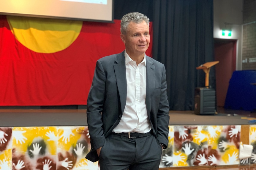 A man in a suit in front of an Aboriginal flag