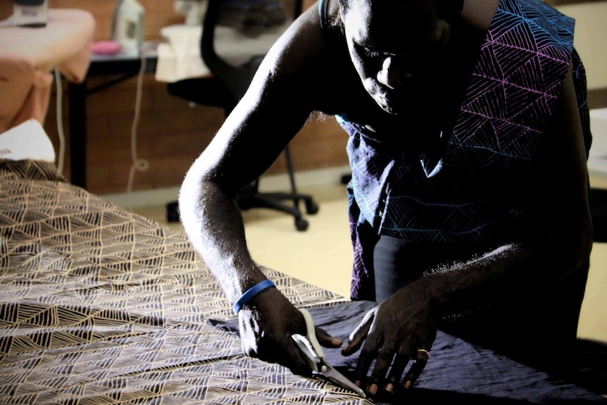 Jamie Timaepatua cuts fabric on a table at the Batchelor Institute.
