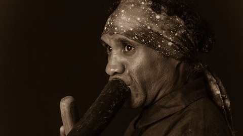 Low key photo of Amos Roach wearing a bandana and playing a Yadaki