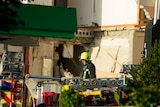 An emergency service worker in helmet and safety gear walks around the ruins of a petrol station. 