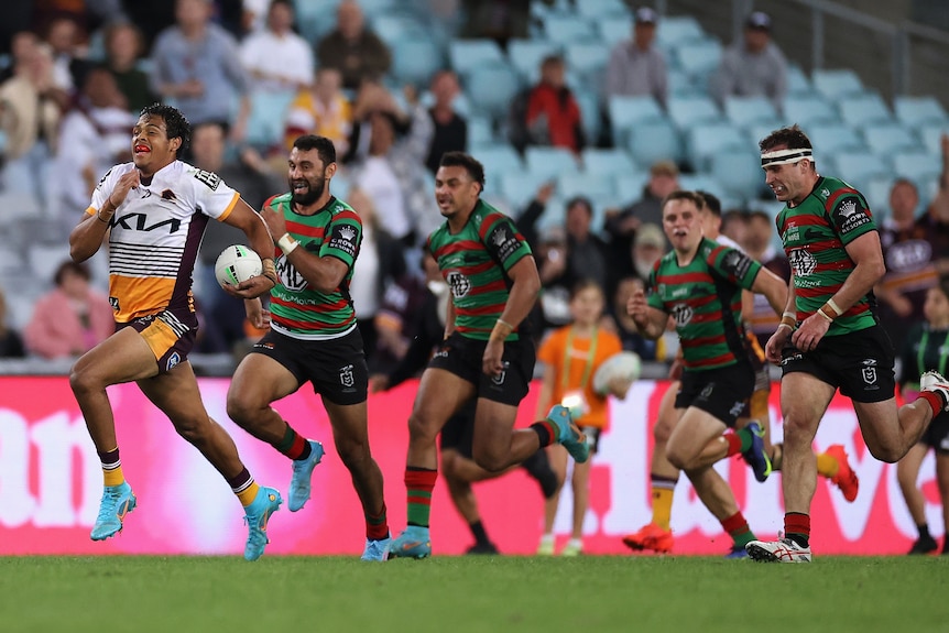 A Brisbane Broncos player sprints downfield with the ball, chased by most of the opposing side.