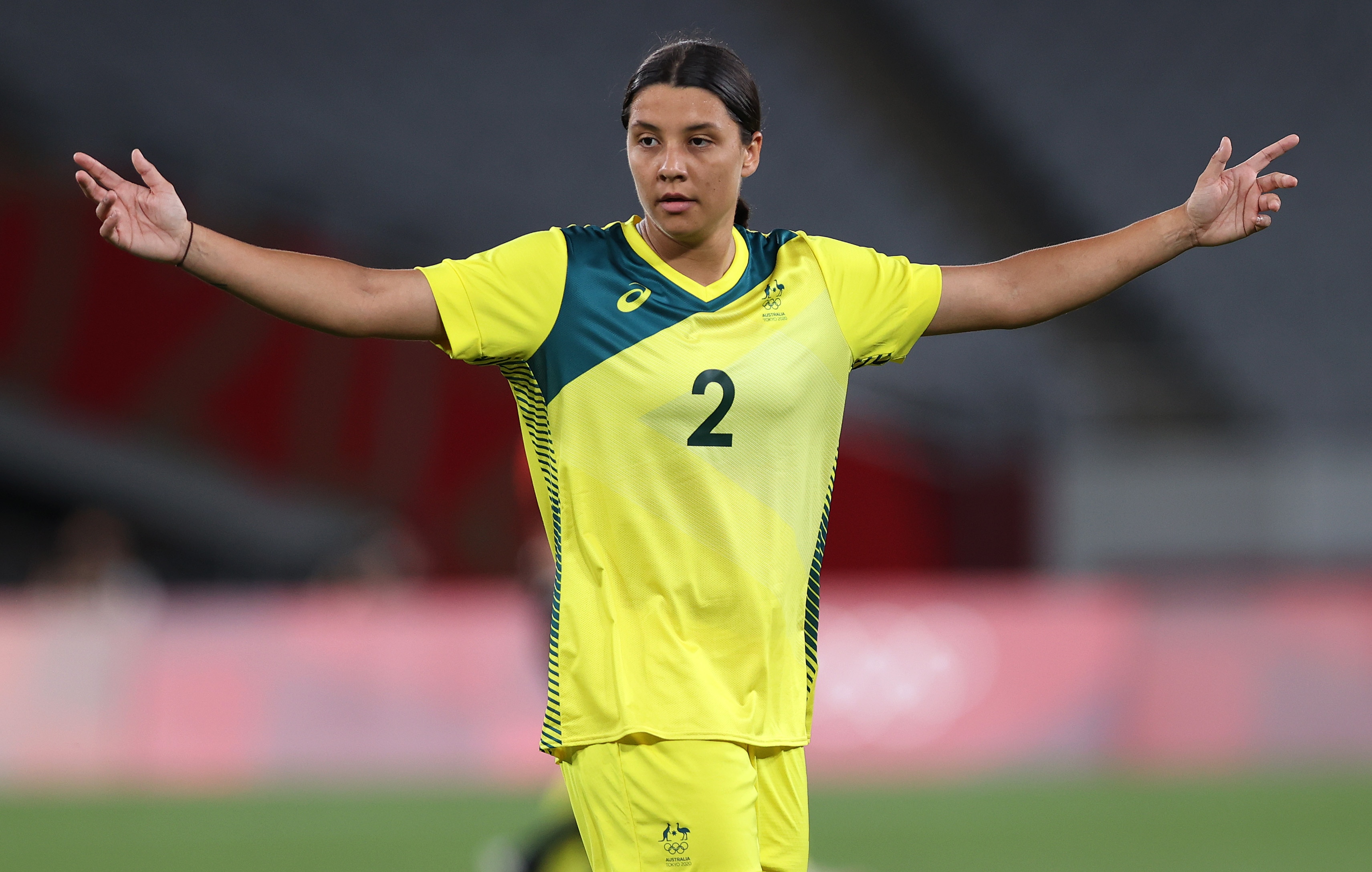 An Australian female football player hols her arms up during a match at the Tokyo Olympics.