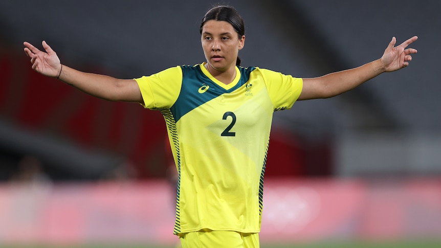 An Australian female football player hols her arms up during a match at the Tokyo Olympics.