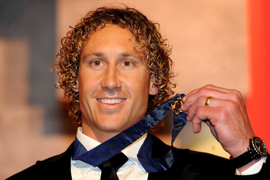 A head and shoulders shot of a smiling Matt Priddis holding his Brownlow Medal around his neck and wearing a suit.