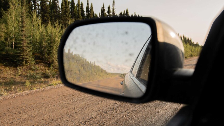 A photo of a dusty Canadian road in a car's rear vision mirror