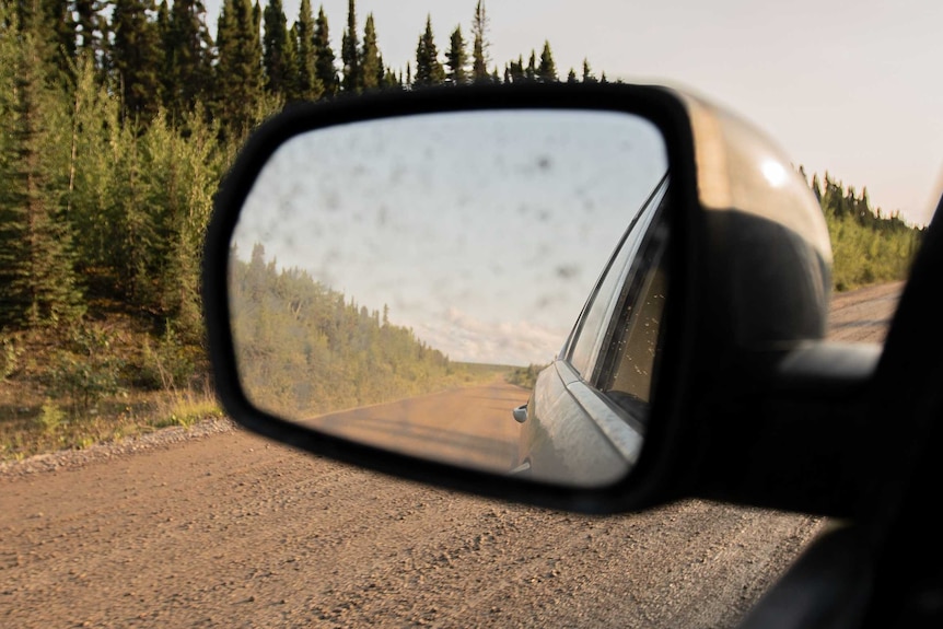 A photo of a dusty Canadian road in a car's rear vision mirror