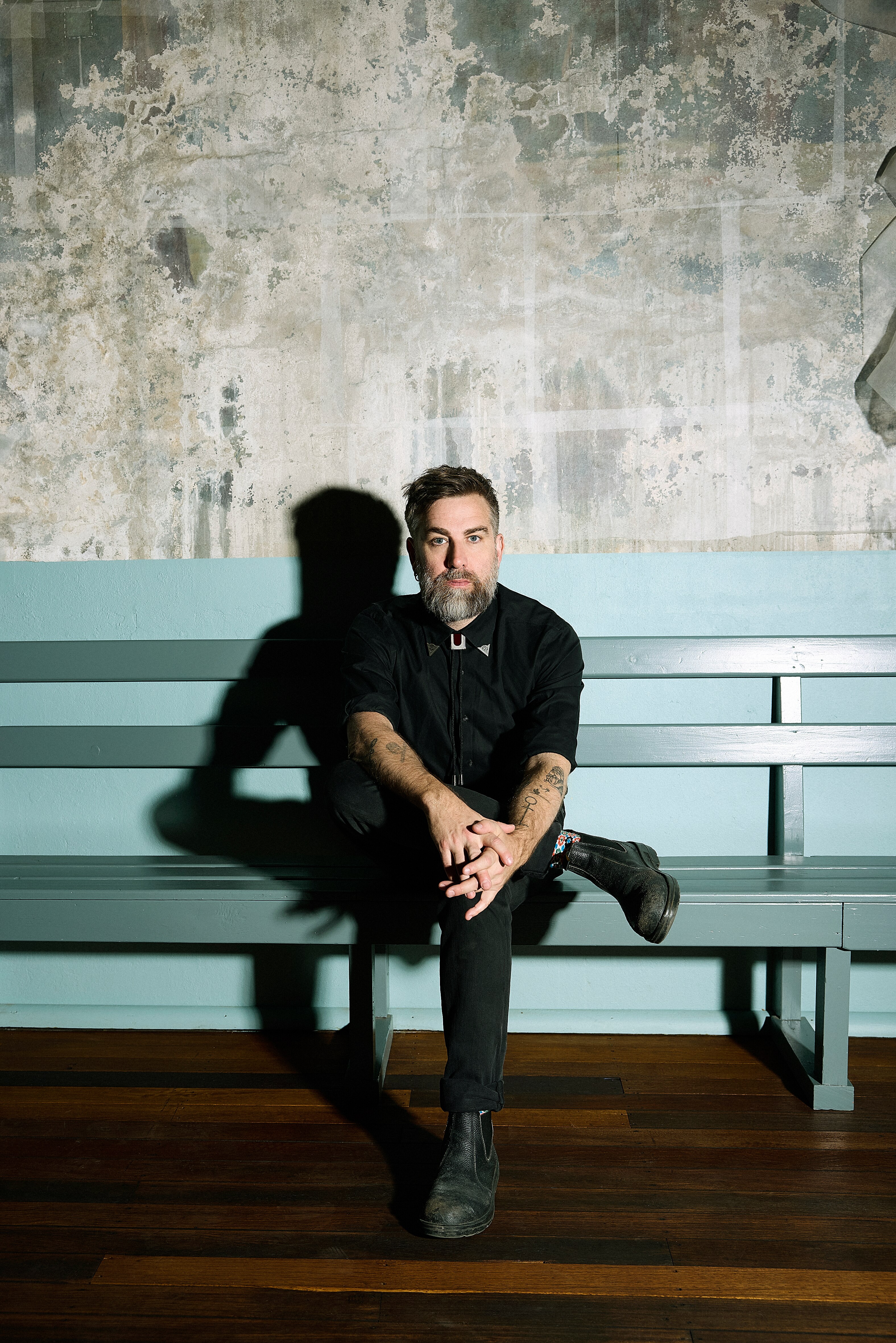 a man with a beard sits on a green bench with his arms folded