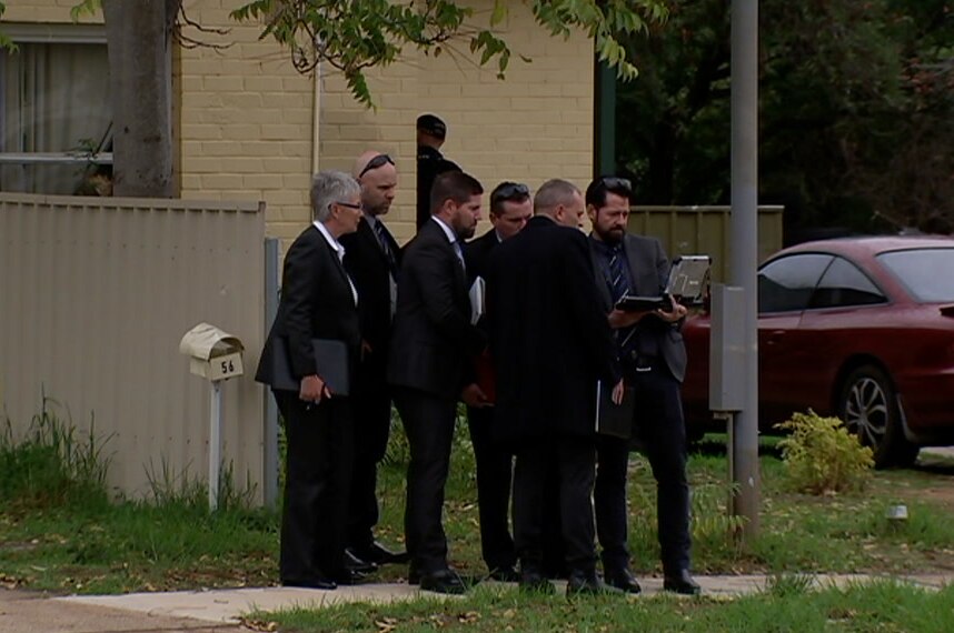 A group of detectives huddle around an ipad in a residential street