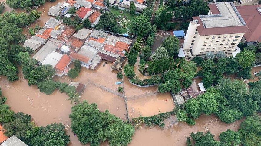 An aerial view shows roofs of homes and cars inundated by muddy water in floods.