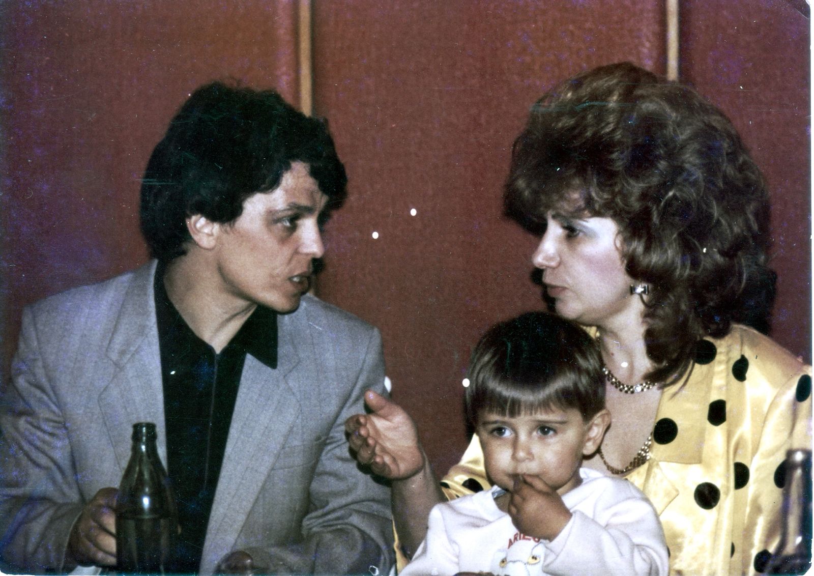 Uma foto antiga de um homem e uma mulher em um jantar com uma criança pequena no colo da mulher. 