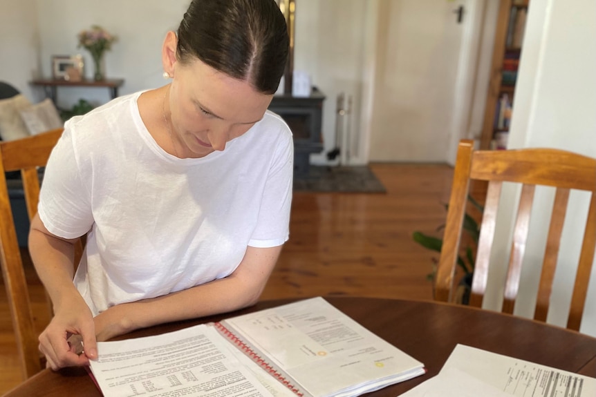 a woman with dark hair sits at a table reading information in a sleeved folder