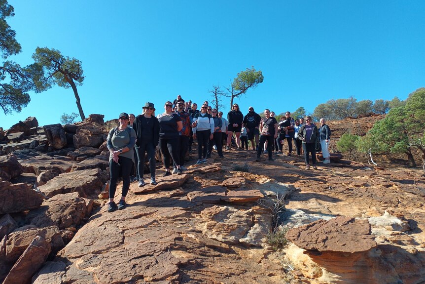 A large group of people stand on top of a large red and yellow rock formation.