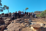 A large group of people stand on top of a large red and yellow rock formation.