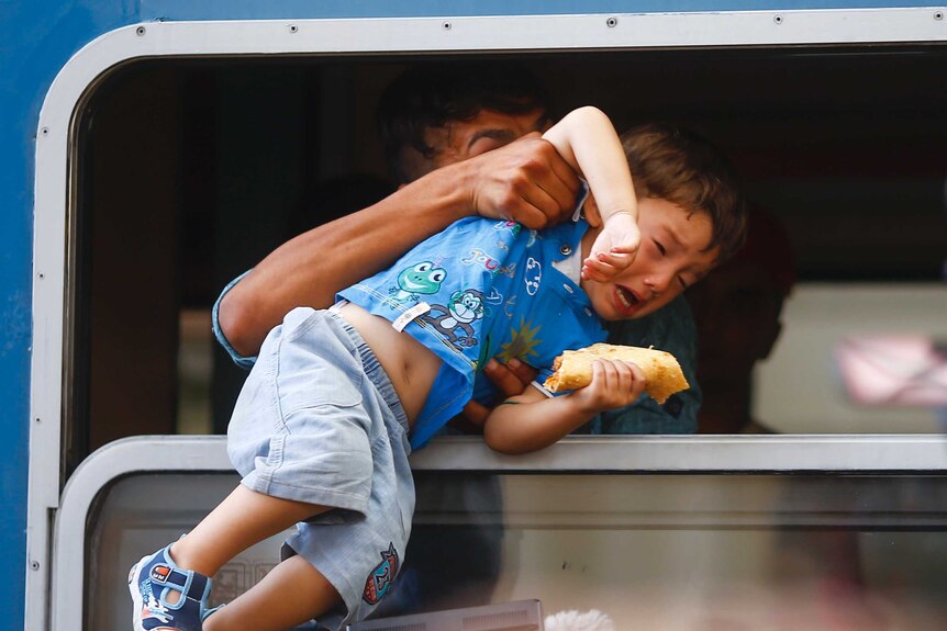 A migrant pulls a boy inside a train