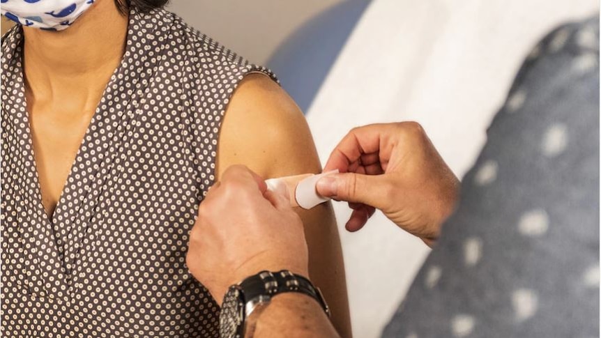  Woman has a band aid stuck to her upper arm by another person.