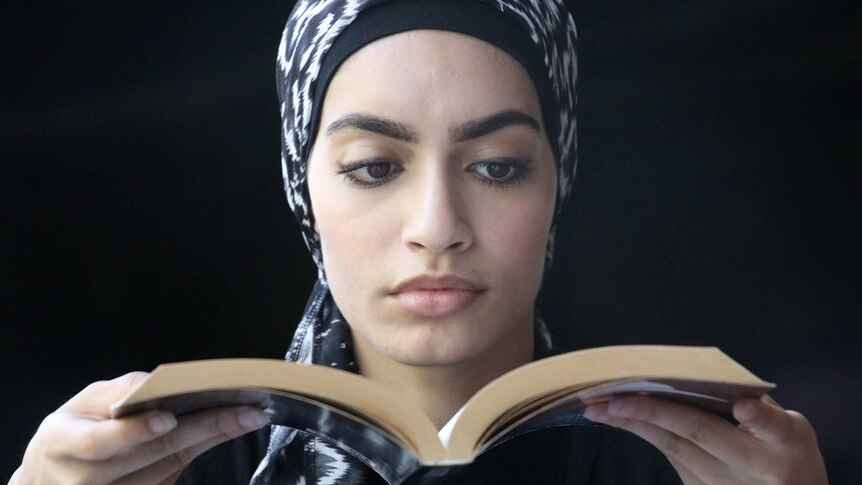 A close-up head and shoulders shot of a young woman wearing a headscarf reading a book.