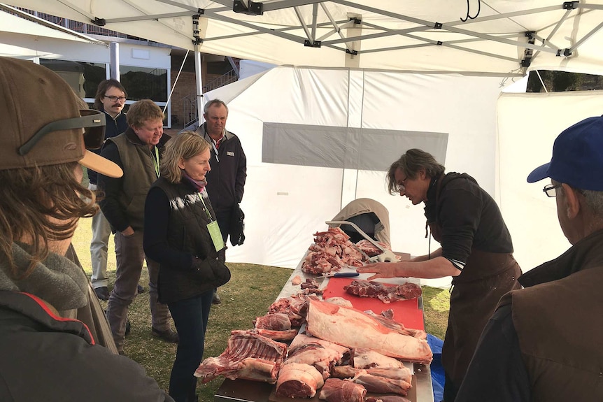 Butcher cuts up carcass as graziers look on.