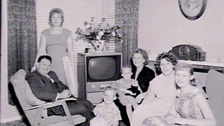 A family posing for a portrait with a television set.